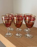 Six ruby red stemmed glasses grouped on wood surface