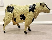 Left side view of painted sheet-metal cow sculpture showing overall form and condition wear