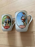 Front view of both ceramic mugs showing artwork and Coca-Cola logos