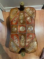 Top view showing leather panels with embossed gold-tone figures and brass end caps