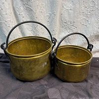 Front view of both brass cauldrons showing size difference and handles