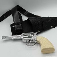 Full view of Daisy cap gun resting in black tooled holster belt