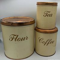 Front view of all three labeled canisters showing cream bodies and copper lids