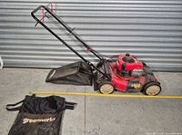 Lawn mower with one catcher bag attached, second Greenworks bag and tape measure showing 21-inch deck