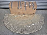 Cardboard shipping box and folded metallic tree skirt displayed on floor