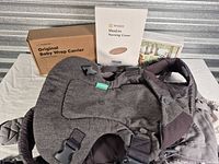 All items front view: Infantino carrier, Ergobaby carrier beneath, boxed wrap carrier, boxed nursing cover