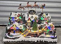 Front view of illuminated animated village showing buildings, tree, moving elements