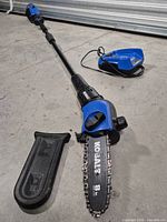 Full view of Kobalt pole saw with battery end, charger, and bar scabbard visible