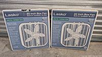 Two boxed Lasko 20-inch fans side by side