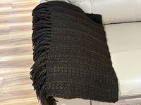Folded brown textured knit throw with fringe displayed on sofa, full view of knit pattern and fringe length