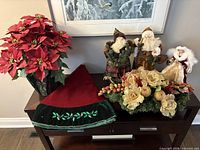 All items arranged on table: poinsettia, two Santa figurines, angel figurine, gold centerpiece, tree skirt