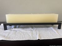 Side view of ivory rectangular candle on black metal stand