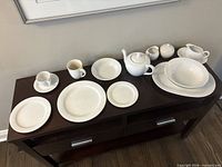 Overview of dinnerware pieces on console table showing plates, cups, teapot, creamer, sugar bowl, serving platter and bowl