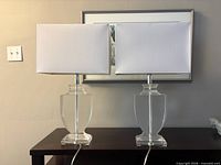 Front view of both acrylic table lamps with shades on dark wood table