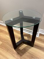 Full view of round glass top side table with brown wood base