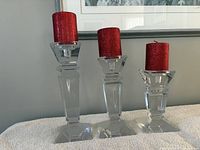 Three clear glass candlestick holders with red pillar candles, showing sizes and condition