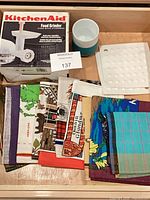 Overview of boxed KitchenAid grinder, stack of tea towels, ceramic tumbler, silicone mat