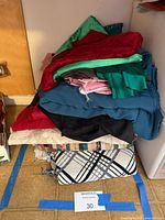 Stack of assorted fabric pieces and plaid throw blanket on floor