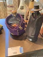 Group of liquor bottles showing black ceramic figure decanter, Crown Royal bottle in purple bag, parts of Galliano and Vandermint bottles