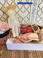 Box showing entire lot: cloth doll, clothes, knit hat, wooden chairs, linens