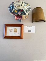 All lot items together: framed cross-stitch, ceramic sewing house, large brass thimble