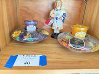 Two scented jar candles with potpourri and figurine displayed on shelf