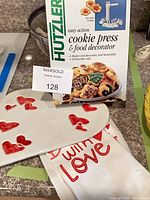Boxed Hutzler cookie press, ceramic heart platter, cotton tea towel visible