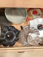 Drawer containing frying pan, bundt pan, steamer basket, lids, baking tray