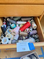 Drawer containing numerous assorted sewing thread spools in various colours and sizes