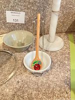 Lot overview showing ceramic bowl, painted wooden spoon, marble paper towel holder, clear glass charger