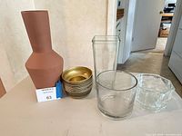Group shot showing terracotta vase, stack of gold metal bowls, tall square glass vase, short cylindrical glass vase, faceted glass bowl