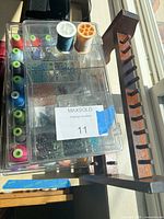 Plastic organizer box with beads, two thread spools on lid, wooden peg rack visible