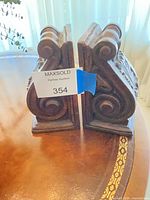 Pair of dark brown carved wood corbels standing upright showing scroll and acanthus leaf details