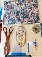 Full view showing framed puzzle, wooden scissors, oval plaque, ceramic lid and knitted piece