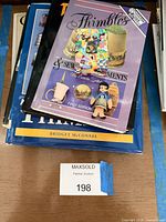 Stacked books showing titles plus thimble doll and patchwork tin