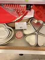 Drawer view showing multiple metal heart pans, red silicone mold, paper doilies, cupcake liners