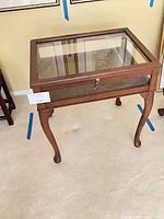 Full view of wooden curio side table with glass top and cabriole legs