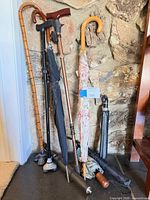 Group of three walking canes and six umbrellas leaning against wall