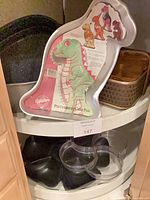Wilton Partysaurus cake pan, black nonstick pans, black and clear plastic bowls visible on shelf