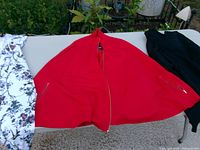 Red cape jacket centered, white floral jacket partial left, black hoodie partial right on table