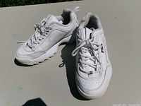 Three-quarter view of both white Fila sneakers showing overall style and condition