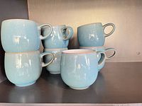 Front view showing all eight aqua glazed mugs stacked