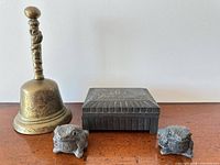 Group view of brass bell, metal trinket box and two stone toads