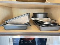 Stack of assorted baking pans on shelf: loaf, square, round, muffin, foil