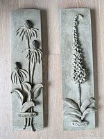 Both concrete botanical plaques side by side showing full designs