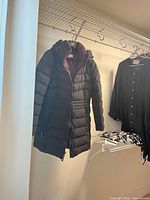 Full view of the black puffer coat hanging to show length and quilted design