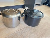 Stainless steel and black speckle pots side by side with lids on