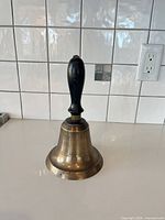Full view of brass bell with black wooden handle