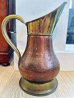 copper pitcher front view showing brass handle, rim, flared spout, hammering