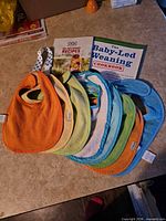 Eight bibs, two books and pacifier clip laid on countertop